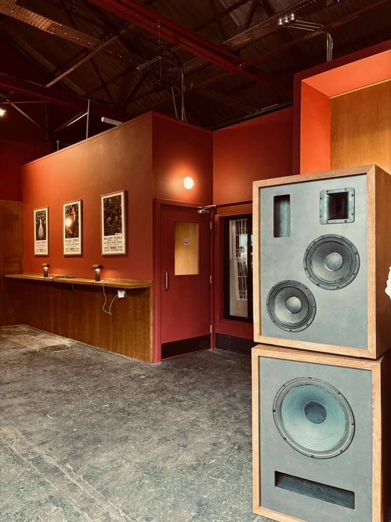 Image of the interior of The Mal Haus brewery. Large speakers and William Morris posters on the wall.
